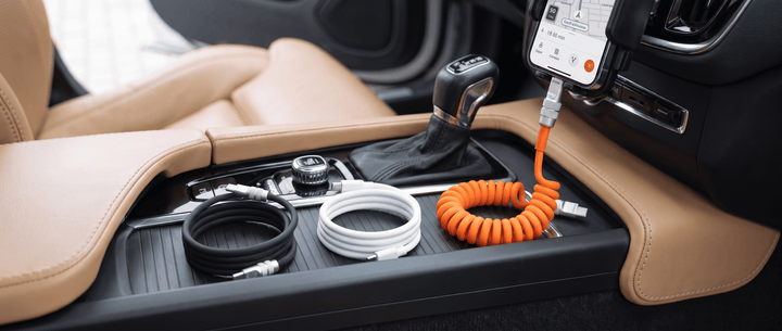 Car center console with three charging cables, including an orange coiled cable plugged into a mounted smartphone.
