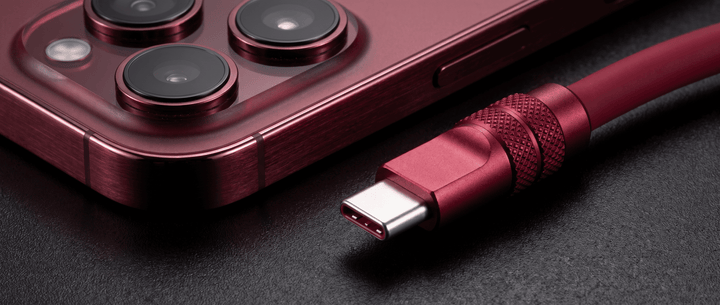 Close-up of a deep cherry red smartphone and a matching USB-C cable connector side by side on a dark textured background.